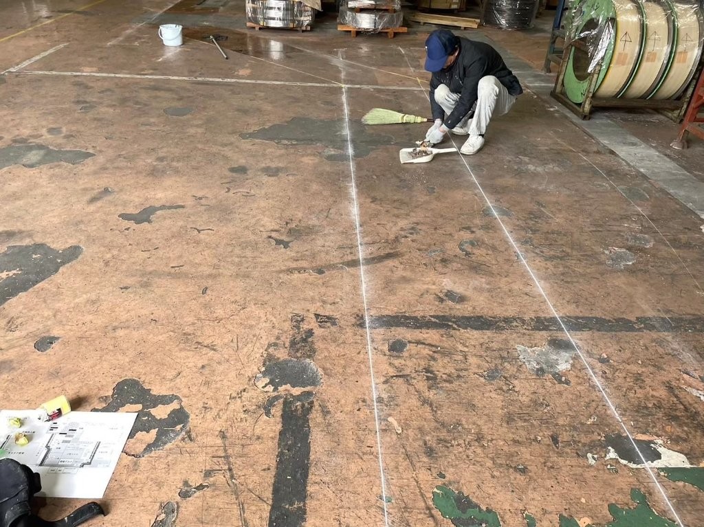 鉄鋼倉庫内で安全通路の墨出し作業を行う様子。チョークラインで通路ラインを正確にマーキング。