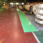 鉄鋼製品が並ぶ倉庫内に施工された緑色の安全通路。塗装仕上がりが明るく、通路が明確に。